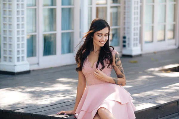 Menina sorridente bonita em vestido rosa sentado em degraus de madeira de café de rua Imagens De Bancos De Imagens