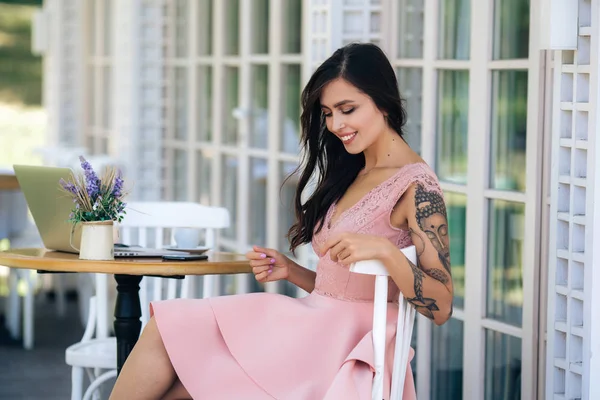 Красивая брюнетка девушка с красивой улыбкой в розовом платье сидит в уличном кафе — стоковое фото