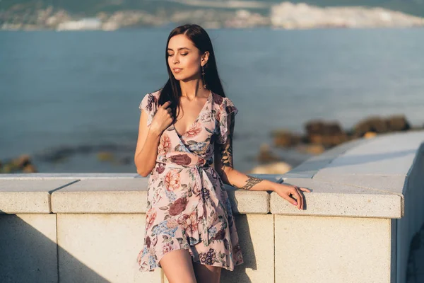 Hermosa chica sonriente en vestido de verano posando al atardecer en el paseo marítimo — Foto de Stock