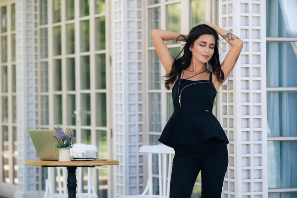 Hermosa chica descansa, posa en la cafetería, portátil y flores en jarrón de pie sobre la mesa — Foto de Stock