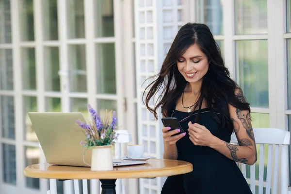 Freiberuflerin mit Tätowierung am Arm nutzt Handy und Laptop für Arbeit im Café — Stockfoto