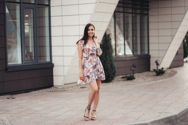 Красивая счастливая молодая женщина в цветном платье позирует возле бизнес-центра — стоковое фото