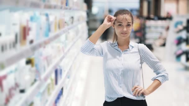 Chica en gafas en la tienda de cosméticos sonriendo y mirando a la cámara, cámara lenta — Vídeo de stock