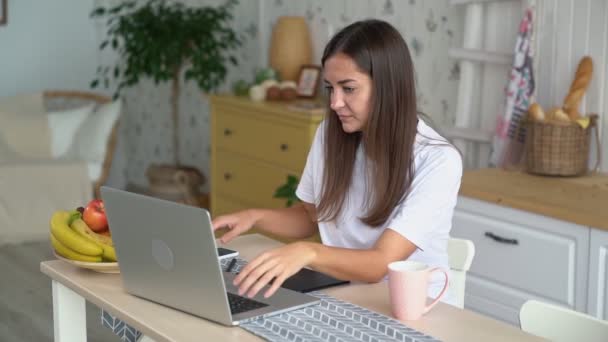 Kız freelancer evde dizüstü bilgisayar ile çalışır, elinde telefon alır, yavaş hareket — Stok video
