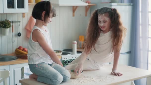 Zwei kleine Schwestern kochen in der Küche, zeichnen mit Mehl auf dem Tisch, Zeitlupe — Stockvideo