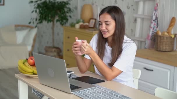 Mujer joven sostiene la taza, lo pone en la mesa, continúa trabajando en el ordenador portátil, cámara lenta — Vídeos de Stock