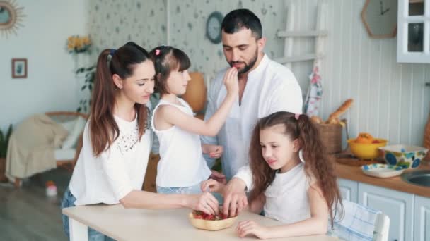 Familia feliz en la cocina, mamá, papá y las hijas comen fresas, cámara lenta — Vídeo de stock