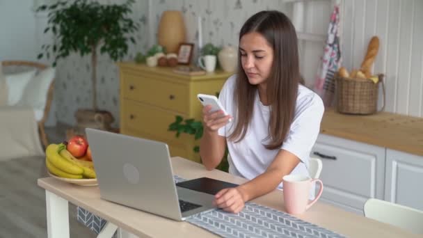 Mujer joven trabaja en el ordenador portátil con la tableta gráfica, toma el teléfono y las llamadas, cámara lenta — Vídeo de stock