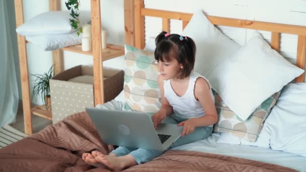 Девочка сидит на кровати, использует ноутбук, эмоционально говорит что-то, замедленная съемка — стоковое видео