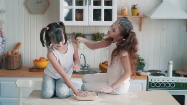 Милые сёстры бросают друг в друга муку, веселятся на кухне, замедленная съемка — стоковое видео