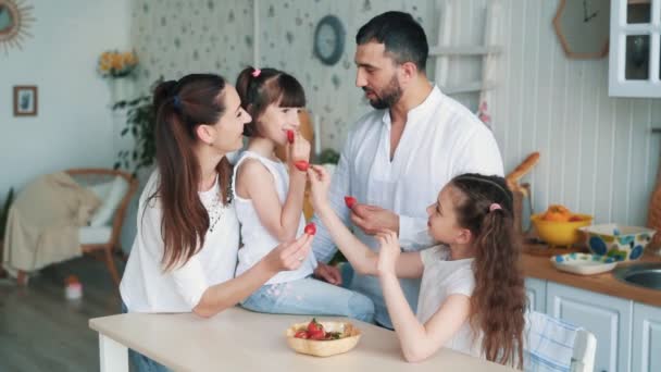 Счастливая семья на кухне, мама, папа и дочери едят клубнику, замедленной съемки — стоковое видео