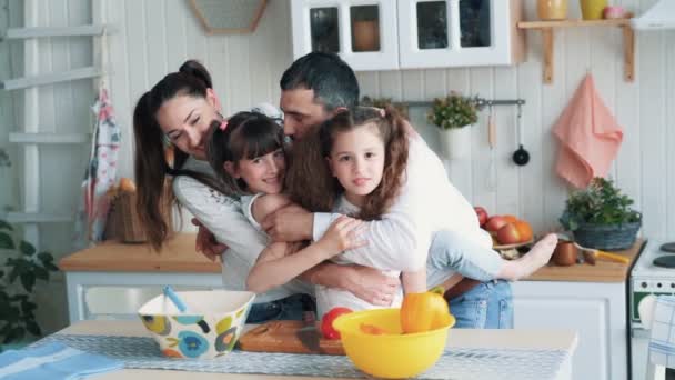 Родители и две дочери готовят на кухне, они обнимаются и смеются, замедленная съемка — стоковое видео