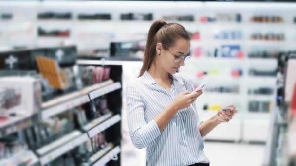 Chica elige rímel y toma una foto en el teléfono en la tienda de cosméticos, cámara lenta — Vídeo de stock