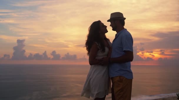 Visão traseira, casal de amantes olhando para o pôr do sol bonito, abraçando, câmera lenta — Vídeo de Stock