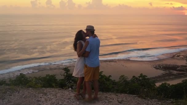 Пара влюбленных обнимаются, целуются на фоне заката и океана, замедленная съемка — стоковое видео