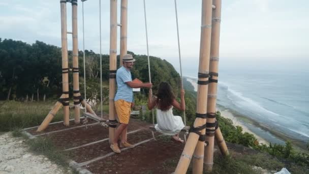 Hombre columpios joven mujer en swing, hermosa vista del océano, cámara lenta — Vídeos de Stock