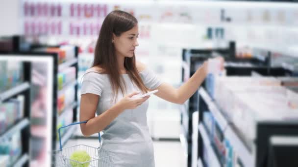 Girl in cosmetics store uses phone, makes photo of selected product, slow motion — Stock Video