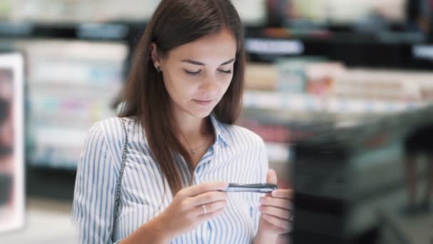 Hermosa chica elige rímel en la tienda de cosméticos, mira la etiqueta, cámara lenta — Vídeos de Stock