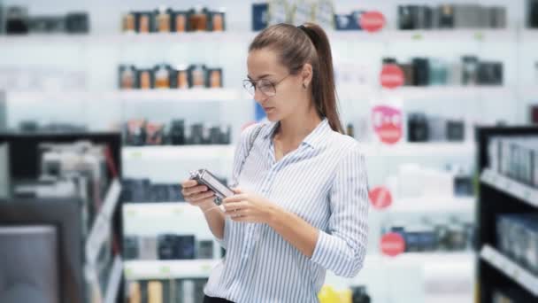 Woman in glasses chooses perfume in cosmetics shop, sniffs it, slow motion — Stock Video