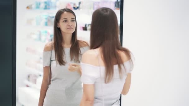 Красивая девушка одевается перед зеркалом в косметическом магазине, замедленной съемки — стоковое видео