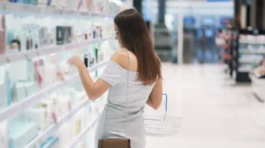Kozmetik dükkanında Pretty kız yüz kremi seçer, sepet, yavaş hareket koyar