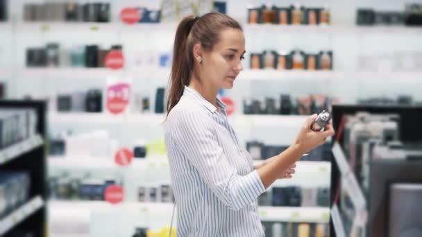 Hübsches Mädchen wählt Parfüm im Kosmetikladen, sprüht es auf Tester, Zeitlupe — Stockvideo