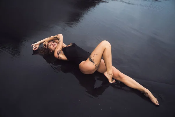 Чувственная сексуальная девушка в купальнике, лежащая на черном песке на берегу океана — стоковое фото