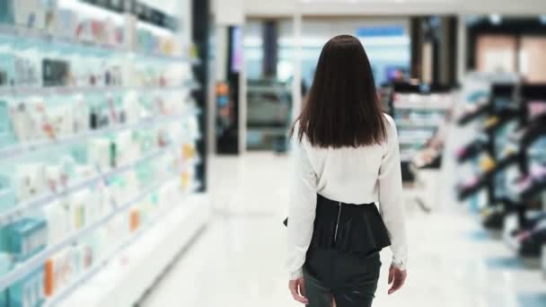 Vue de derrière, la femme va au magasin de cosmétiques le long des étagères, au ralenti — Video