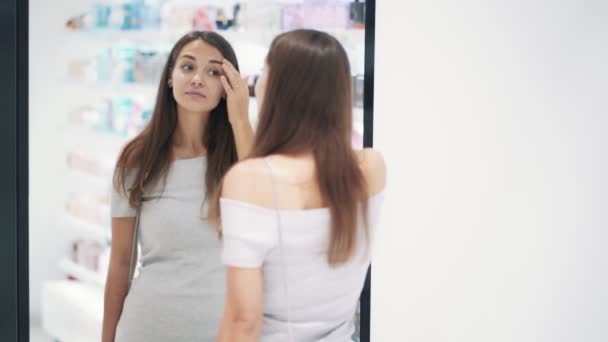 Красивая девушка одевается перед зеркалом в косметическом магазине, замедленной съемки — стоковое видео