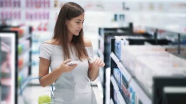 Ticaret mağazasında güzel kız telefon kullanır ve kozmetik, yavaş hareket seçer