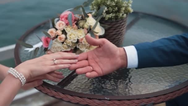 Gros plan marié tient mariée par bras assis à la table, bouquet nuptial sur le fond — Video