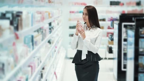 Happy woman chooses perfume in cosmetics store, sprays it on tester, sniffs it — Stock Video