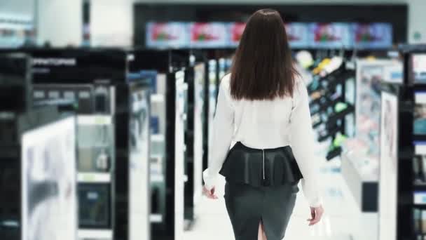 Вид сзади, женщина идет в магазин косметики между полками, замедленная съемка — стоковое видео
