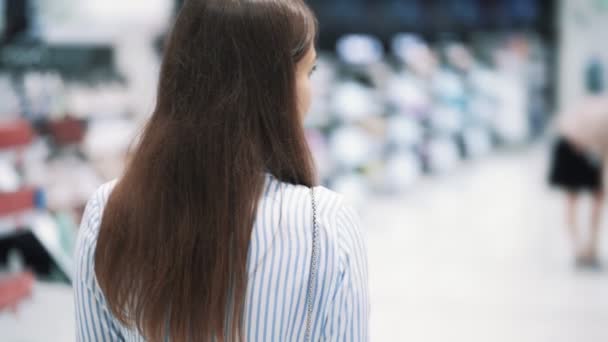 Vista trasera, la mujer va entre estantes en la tienda de cosméticos, cámara lenta — Vídeos de Stock