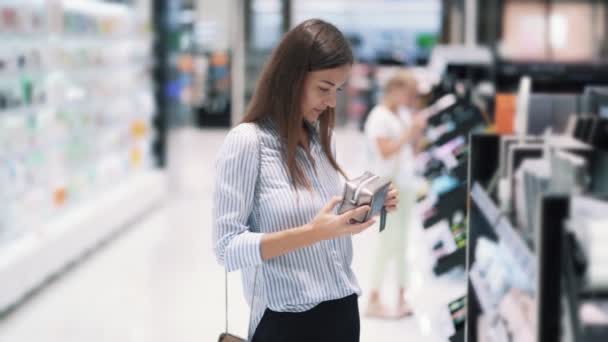 Hermosa joven mujer elige bolsa de maquillaje en la tienda de cosméticos, cámara lenta — Vídeos de Stock