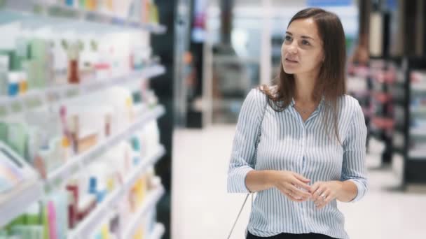 Hermosa mujer va entre estantes en la tienda de cosméticos, cámara lenta — Vídeos de Stock