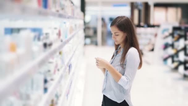 Junge Frau im Kosmetikladen wählt Creme, liest Etiketten, Zeitlupe — Stockvideo