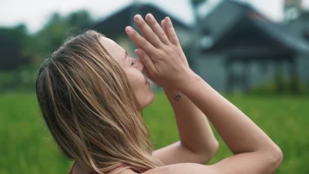 Vista lateral, retrato de una joven haciendo ejercicios de yoga, vegetación sobre fondo — Vídeo de stock