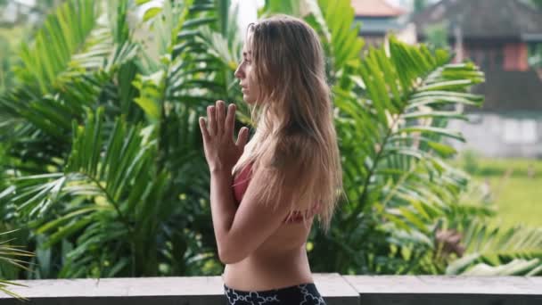 Giovane donna che pratica yoga, che si estende sul balcone con verde sullo sfondo — Video Stock