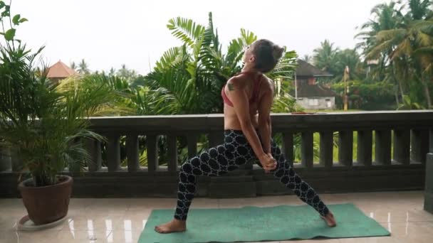 Mujer fitness disfrutando practicando yoga en balcón con palmeras en el fondo — Vídeos de Stock