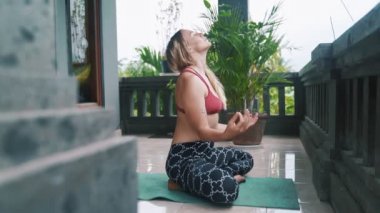 Genç kadın yoga egzersizleri yapıyor, meditasyon ve veranda yoga minderi üzerinde dua