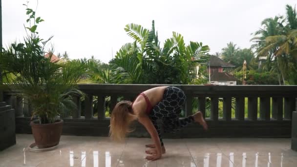 Junge Frau übt Yoga-Pose auf Balkon mit Palme im Hintergrund — Stockvideo