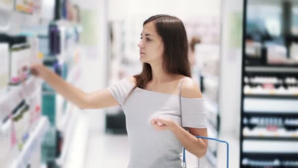 Jeune femme dans le magasin de cosmétiques choisit le shampooing, lit l'étiquette, ralenti — Video