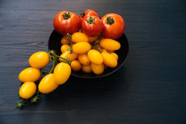 Ahşap arka planda siyah kase içinde sarı ve kırmızı kiraz domates üst görünümü