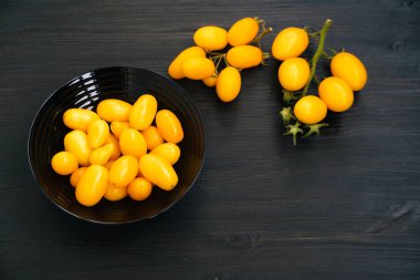 Üst görünüm, siyah ahşap arka plan üzerinde kase sarı kiraz domates, kopya alanı