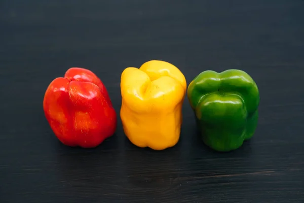 Bovenaanzicht van rode, gele, groene paprika op zwarte houten achtergrond — Stockfoto