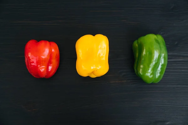 Top view of red, yellow, green bell peppers on black wooden background — Stock Photo, Image