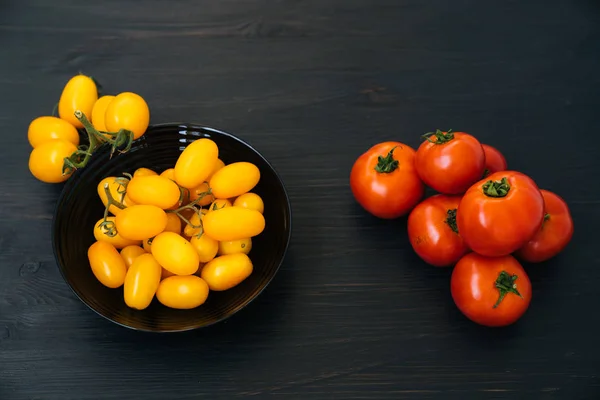Top view of yellow and red cherry tomatoes in black bowl on wooden background Royalty Free Stock Photos