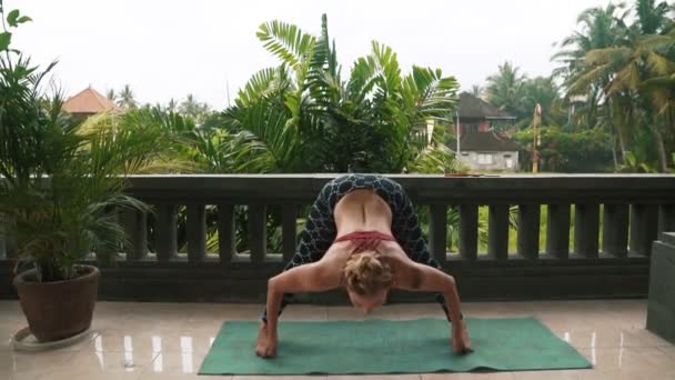 Vrouw doet yoga oefeningen op balkon op yoga mat met groen op achtergrond — Stockvideo