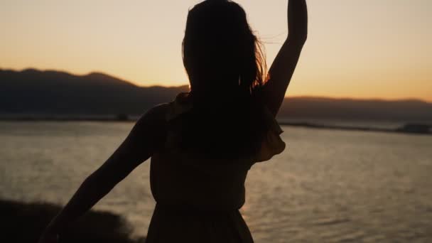 Silhouette of woman looks at sunset on beach, opens her arms wide, slow motion — Stock Video